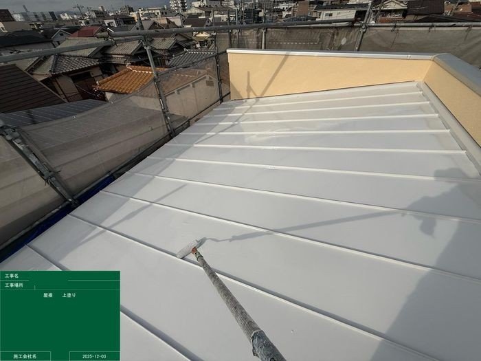 K様邸金属屋根の上塗り作業中。白色の上塗り塗料がローラーで全面に塗り広げられている